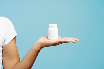 Woman hand holding white plastic pill bottle on blue background