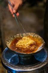 Sapporo ramen noodle lifted up by red chopsticks with steam against black background