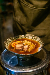 Sapporo ramen noodle lifted up by red chopsticks with steam against black background