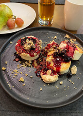 cakes drizzled with cherry sauce on a round tray, a pear with grapes on a white round plate, a white coffee mug and a glass of apple juice.