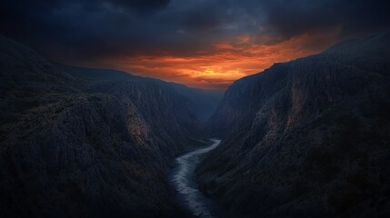 A river winds through a dramatic canyon, with an orange sunset illuminating the clouds above.