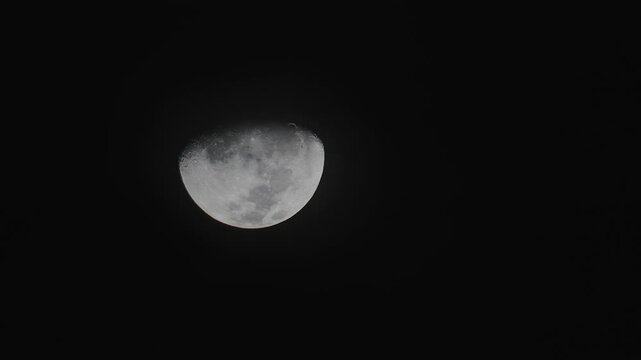 Timelapse of the waxing moon as it is moving acroww the sky, with clouds obstructing it ocassionally.