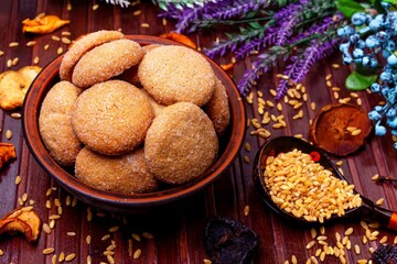 homemade cookies in a clay plate, wheat in a spoon, dried fruits, herbs and berries on a brown background