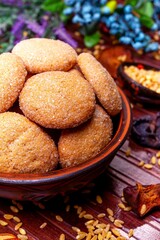 homemade cookies in a clay plate, wheat in a spoon, dried fruits, herbs and berries on a brown background