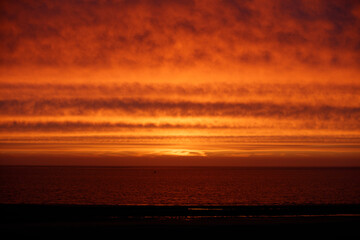 Fiery sunset over a calm ocean.  Dark, silhouetted shoreline.