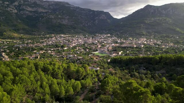 Picturesque aerial view of Soller, a charming town in Mallorca, nestled between lush greenery and dramatic mountain ranges at sunset