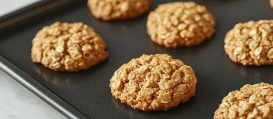 Burnt oatmeal cookies on a black baking sheet showcasing a disappointing baking outcome with a focus on texture and color contrast.