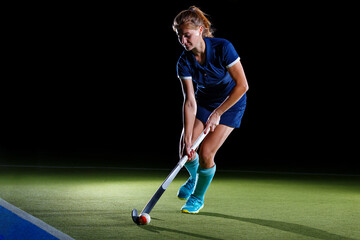 Competitive female hockey player practices on a lit field during night