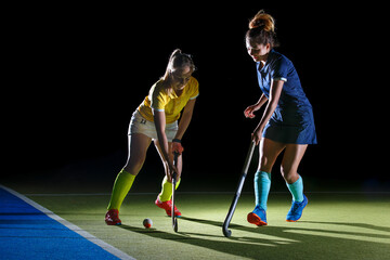 Two field hockey players compete in an intense match under contrast studio light