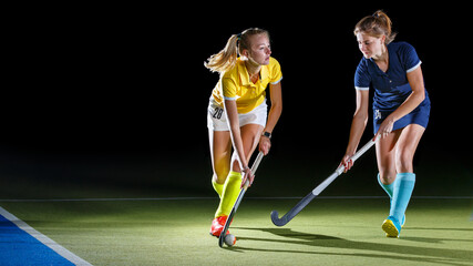 Two field hockey players compete in an intense match under studio lights