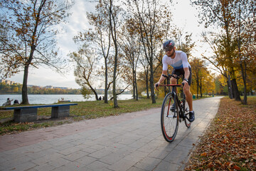 Naklejka premium Triathlete riding along a lakeside path in autumn foliage during daytime