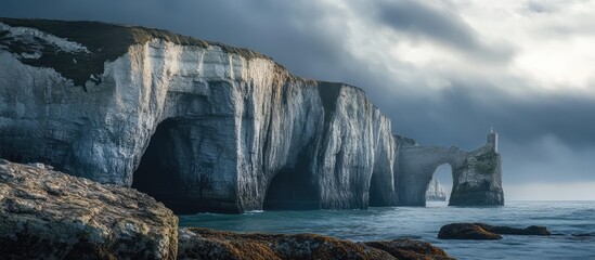 Chalk cliffs with natural arch and stone needle along a serene coastline under dramatic cloudy sky...