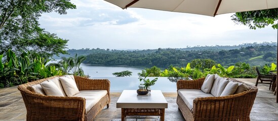 Outdoor lounge area with rattan chairs and coffee table beneath an umbrella overlooking a serene lake and lush greenery