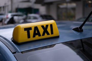 A close up of a yellow taxi sign mounted on the roof of a blue car.