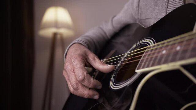 Guitarist and music concept. Elderly man plays an acoustic guitar sitting in the living room. Man's hands playing melody.