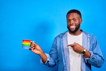 Smiling young man showing colorful mug and pointing finger on blue background