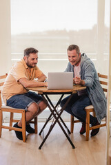 Gay couple using laptop at home smiling and having fun