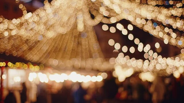 Defocused blurred Christmas background view of winter city street decorated with festive lights New Year's illumination decorations and unrecognizable people crowd walking through xmas market