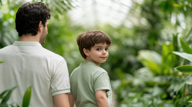 A father and son explore a lush greenhouse filled with vibrant greenery, enjoying nature together in a serene setting.