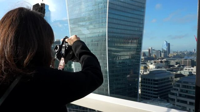 Woman photographs London's skyline from a rooftop with modern glass buildings in background