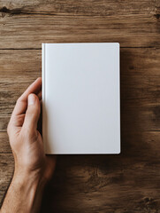 Fototapeta premium A blank notebook held in a hand on a wooden surface.