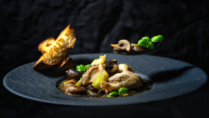 Homemade food for dinner, mushrooms with quail meat and spices. On a black plate on a dark background. Restaurant.