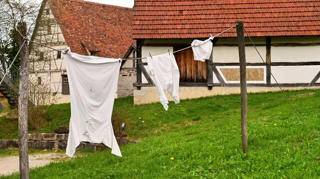 Row of ancient clothes is hanging on a clothesline outside. The clothes are freshly washed and are drying in the wind. Shirt Underpants and bra