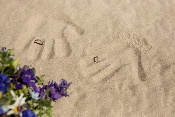 Handabdrücke im Sand mit Eheringen und Blumenstrauß bei einer Strandhochzeit