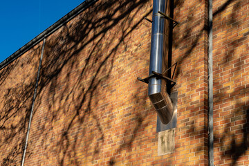 A shiny metal pipe extends from a brick wall, with intricate shadows cast on the surface. The...