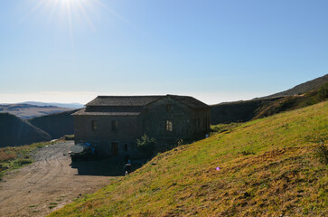 A building situated on a hill, surrounded by grass, with a clear sky and mountainous background reflecting a rural landscape