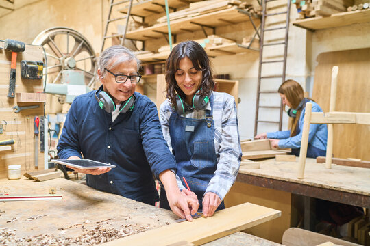 Experienced craftsman teaching young apprentice in a busy lumber workshop