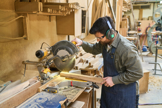 Focused woodworker using a table saw in a busy lumberyard