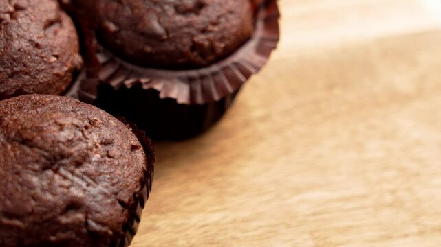 Hand picking up a freshly baked chocolate cupcake with cocoa texture in brown paper liner from a pile. Organic muffins