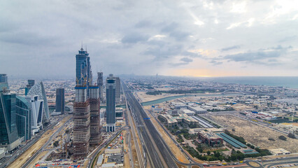 Dubai's business bay towers before sunset timelapse. Rooftop view of some skyscrapers and new towers under construction.