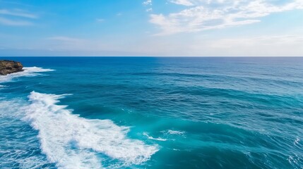 Obraz premium Ocean waves crashing on a rocky shore under a bright blue sky.