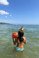 Kids playing in shallow sea water with ball, summer fun.
