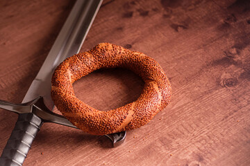 Freshly baked simit resting beside a medieval sword, creating a juxtaposition of old and new. Still life image with a Turkish simit and a sword.