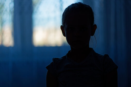 A young girl is standing in a dark room with a window behind her. Nizhny Novgorod. Russia
