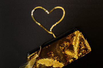Flat lay of a gold sequins pencil case,  black paper background. Little gold tassel hanging down. Concept of Valentine's Day gifts, wedding proposal.
