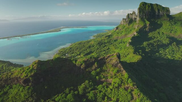Aerial drone footage of stunning beauty Bora Bora tropical island, green forest vegetation, turquoise lagoon, and majestic mount Otemanu under a clear blue sky. Wild travel destination, remote nature