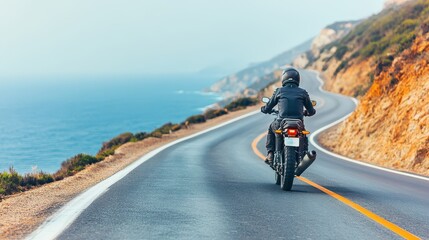 Obraz premium A motorcyclist rides along a scenic coastal road, enjoying the ocean view and the beauty of nature on a sunny day.