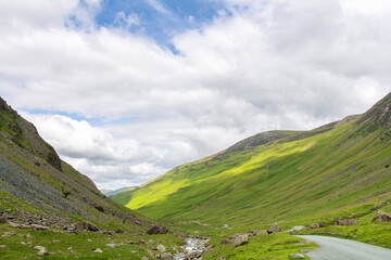 Descend of the B5289 road with steep grade from Honister Pass in the Lake District, Cumbria, UK surrounded by green mountains with pasture