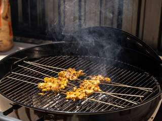 Grilling skewered meat on a smoky charcoal barbecue in bright sunlight