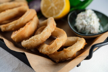 crispy fried calamari rings , golden brown crusty finger food served with dip sauce, greens and lemon, styled on plate with cooking paper
