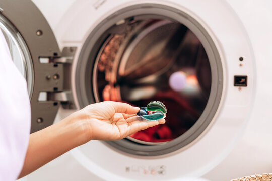 Housewife holding laundry detergent pod in front of washing machine