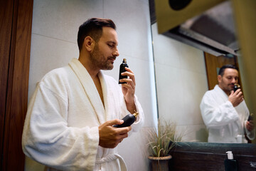 Smiling man smelling perfume bottle in bathroom.