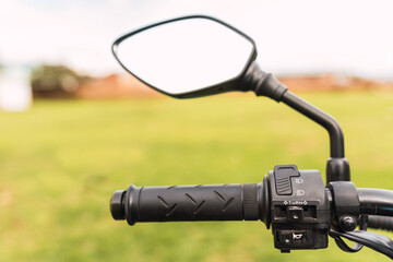 Black motorcycle rearview mirror and motorcycle handlebar on a sunny day of travel