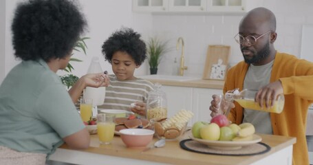 Perfect African American family having tasty healthy breakfast sitting around table in kitchen talking enjoying food. Domestic life and nutrition concept.