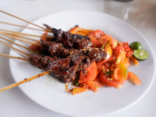 delicious beef satay served with tomato and chili pieces on white plate