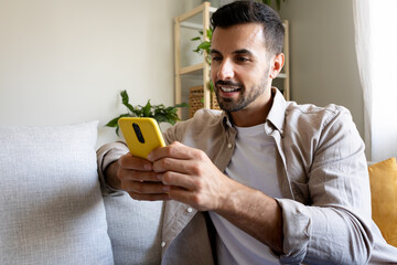 Relaxed caucasian man using smart phone at home sitting on the couch.